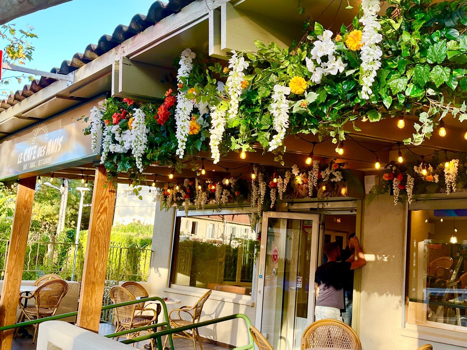 Terrasse du Café des Amis à Toulon décorée d'une cascade de glycines et fleurs artificielles blanches, orange et rouges