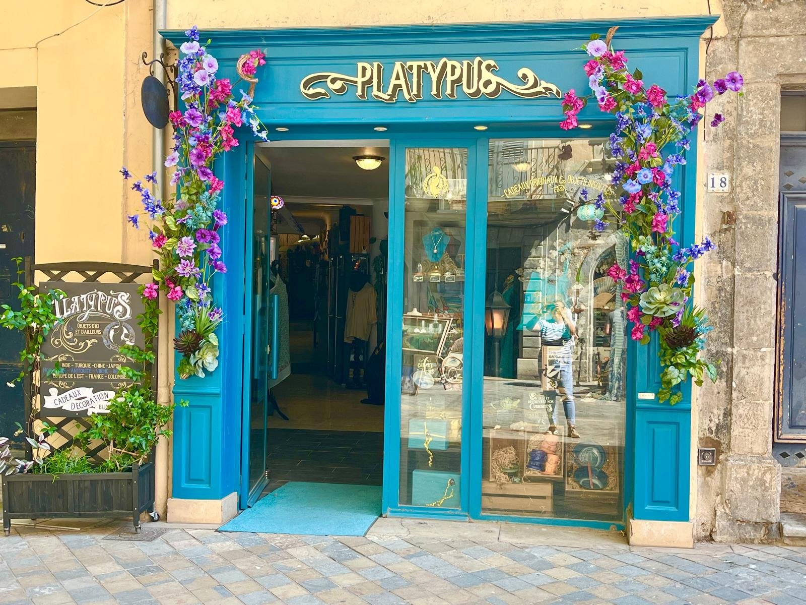 Devanture bleue de la boutique Platypus à Toulon ornée de fleurs artificielles roses, violettes et bleues