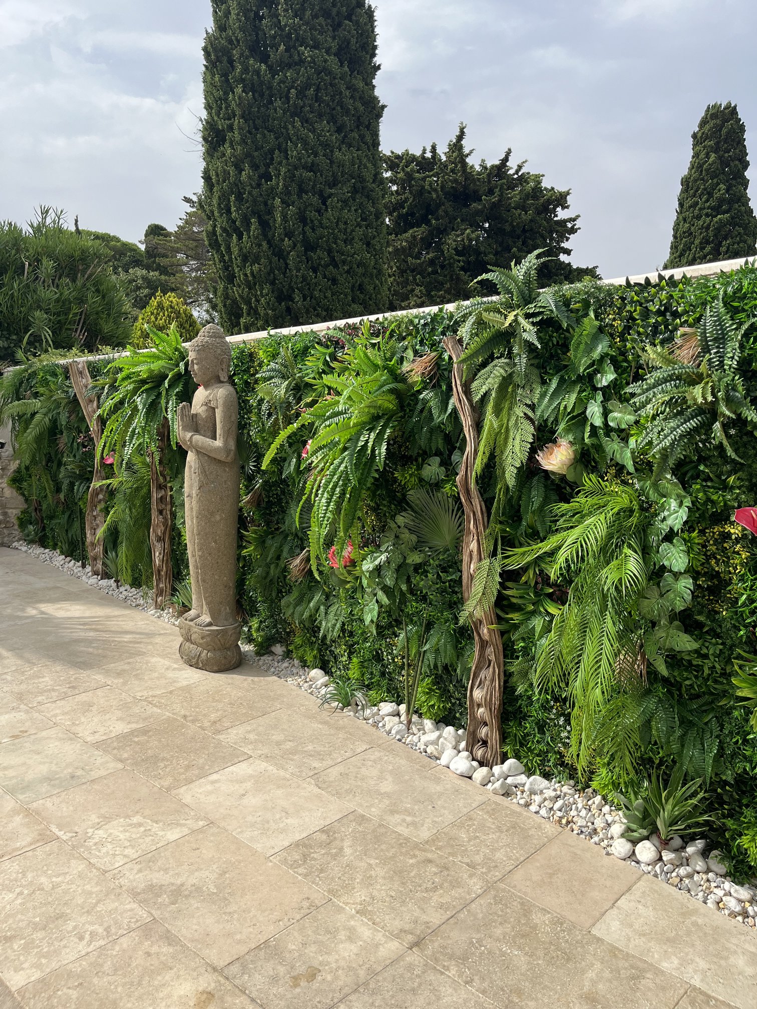 Allée bordée d'une haie végétale artificielle fleurie et d'une statue de Bouddha, jardin privé