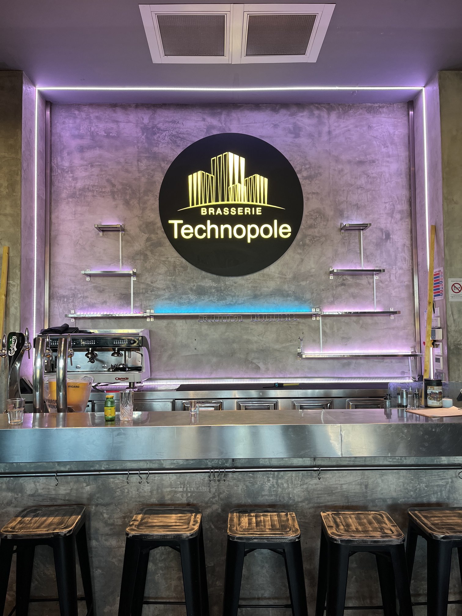 Bar rétroéclairé avec logo Brasserie Technopole encadré de végétation artificielle et de LED violettes