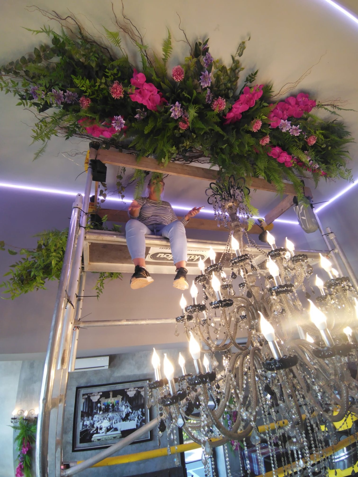 Installation d'une composition suspendue de fleurs roses et mauves au-dessus d'un lustre en cristal, restaurant La Technopole