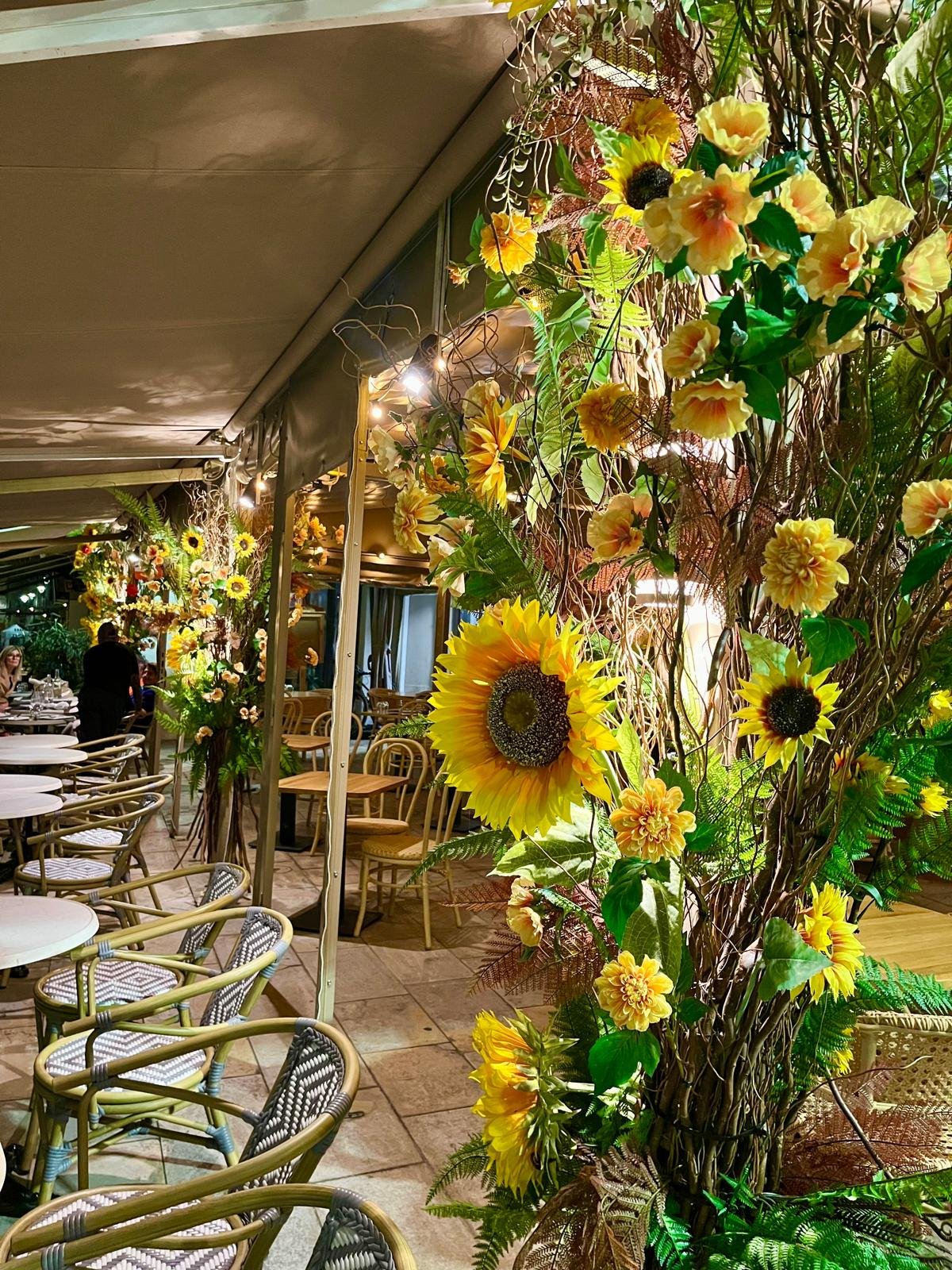 Grande composition de tournesols et dahlias artificiels jaunes et oranges sur la terrasse d'un restaurant