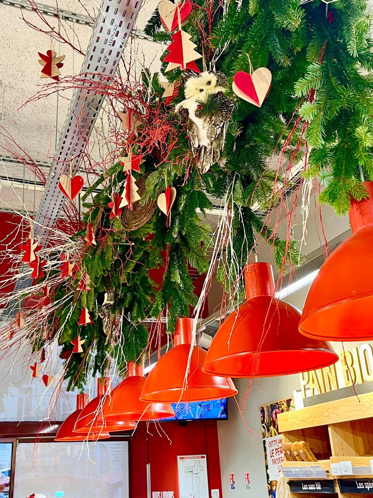 Suspension de Noël en branches de sapin, cœurs en bois et hibou décoratif au plafond d'une boulangerie
