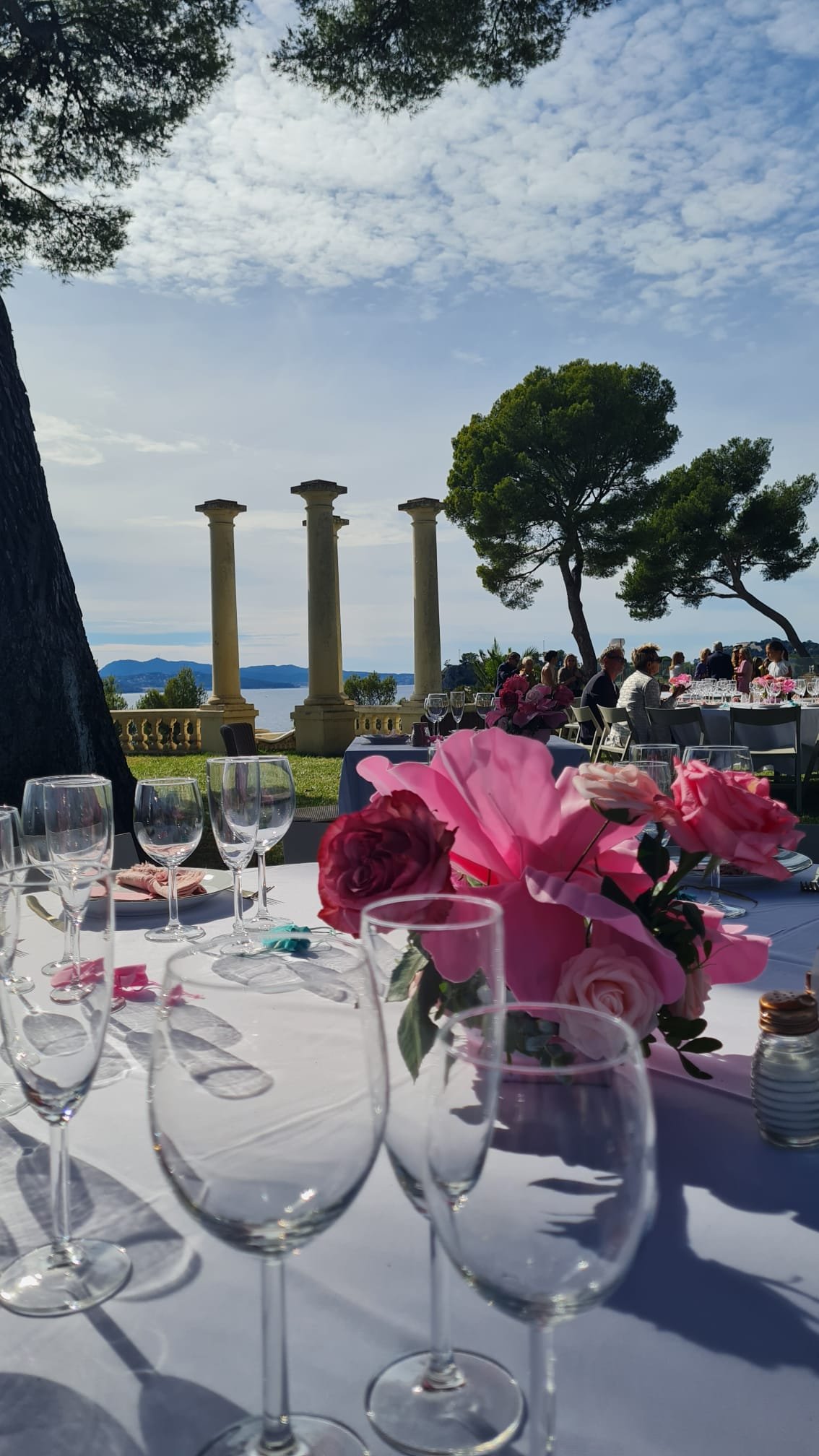 Table de mariage décorée de roses roses sur une terrasse face à la mer, colonnes en pierre en arrière-plan