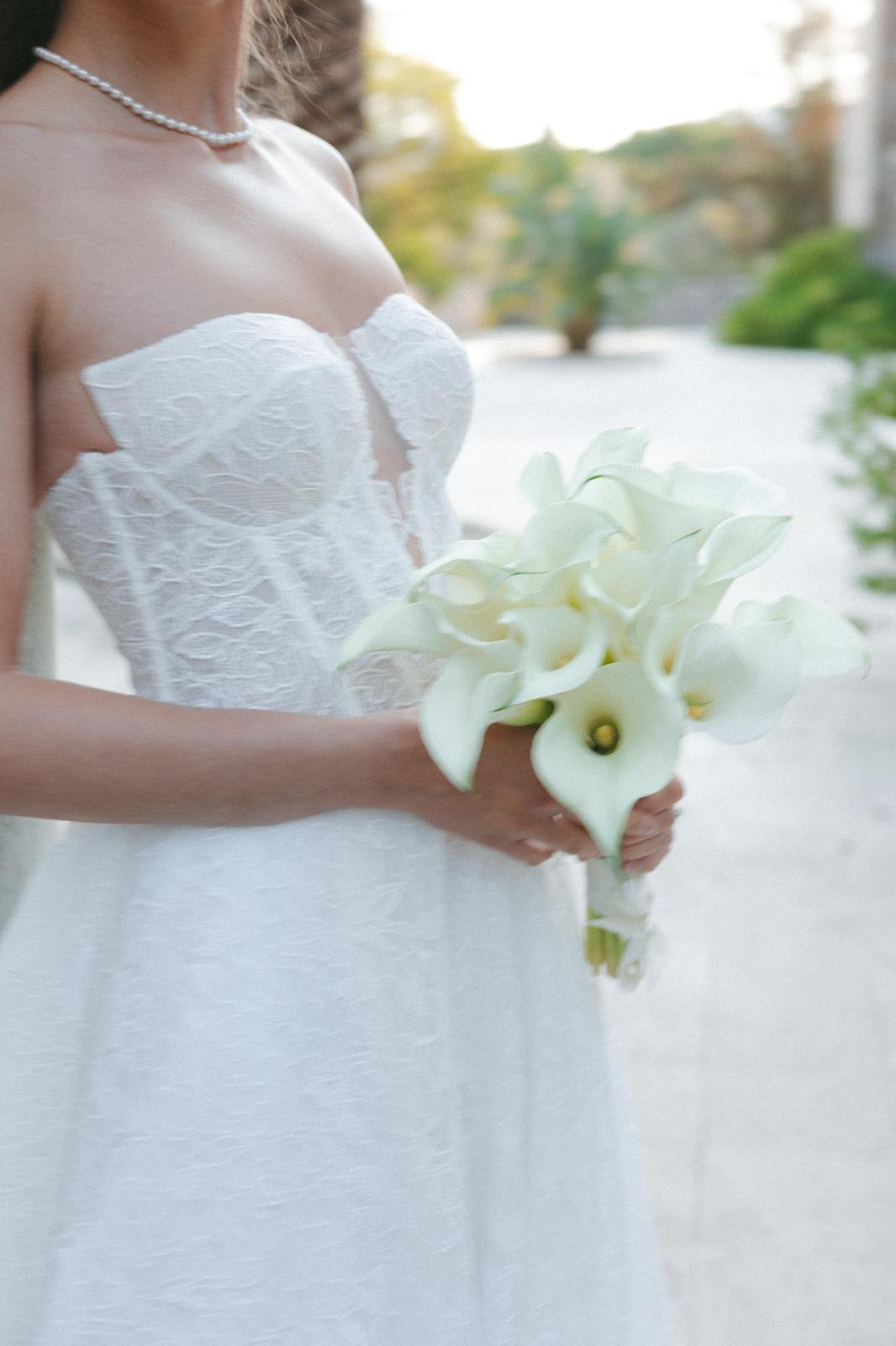 Bouquet de mariée en arums blancs tenu contre une robe de dentelle