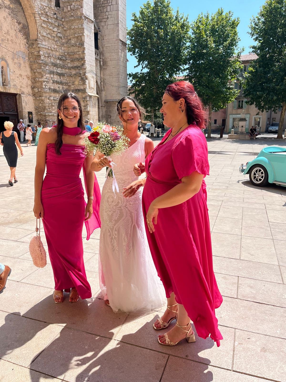 Mariée et demoiselles d'honneur en robes fuchsia avec bouquet coloré devant une église en pierre