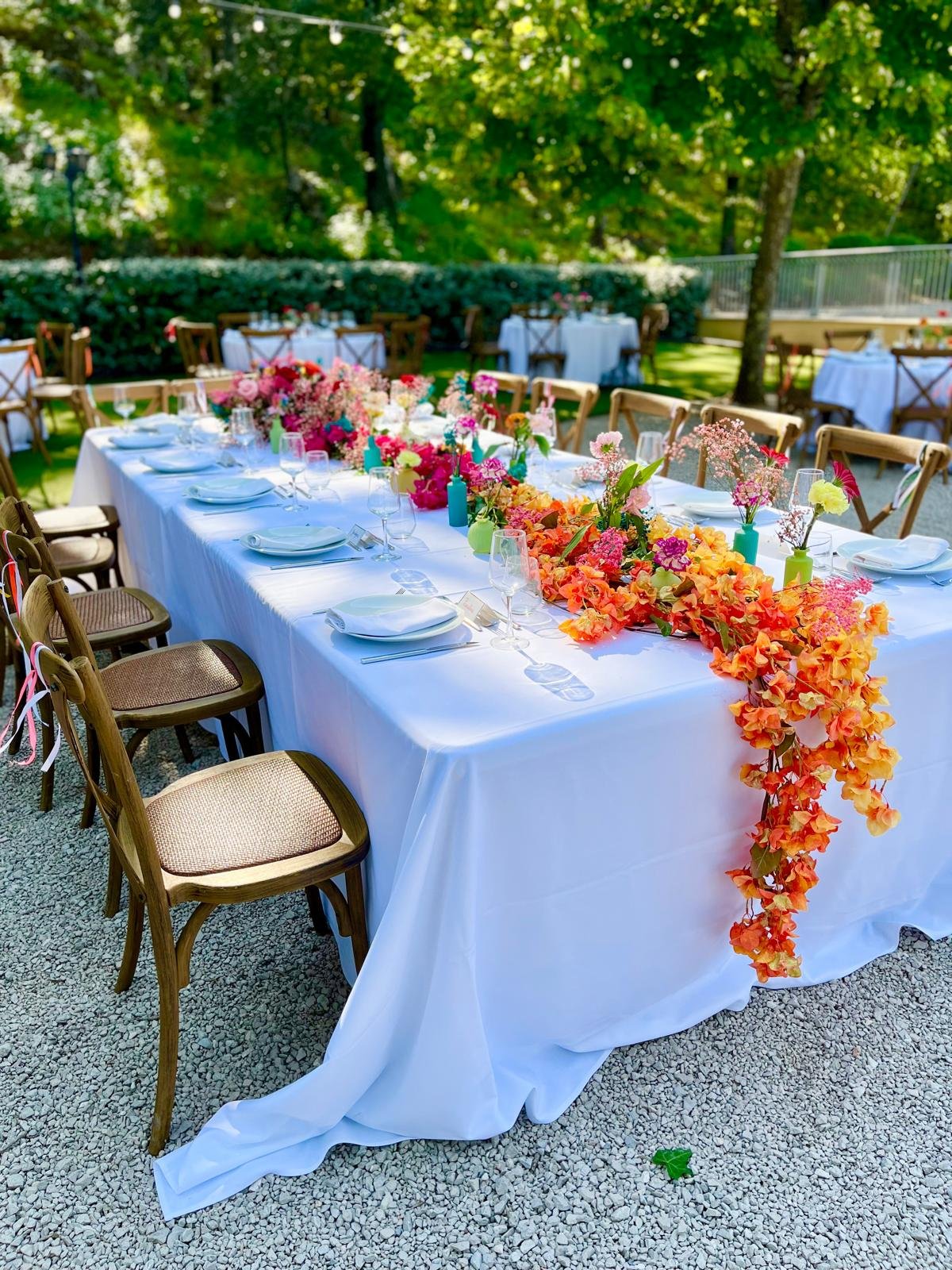 Table de mariage décorée d'une cascade de fleurs orange et roses dans un jardin