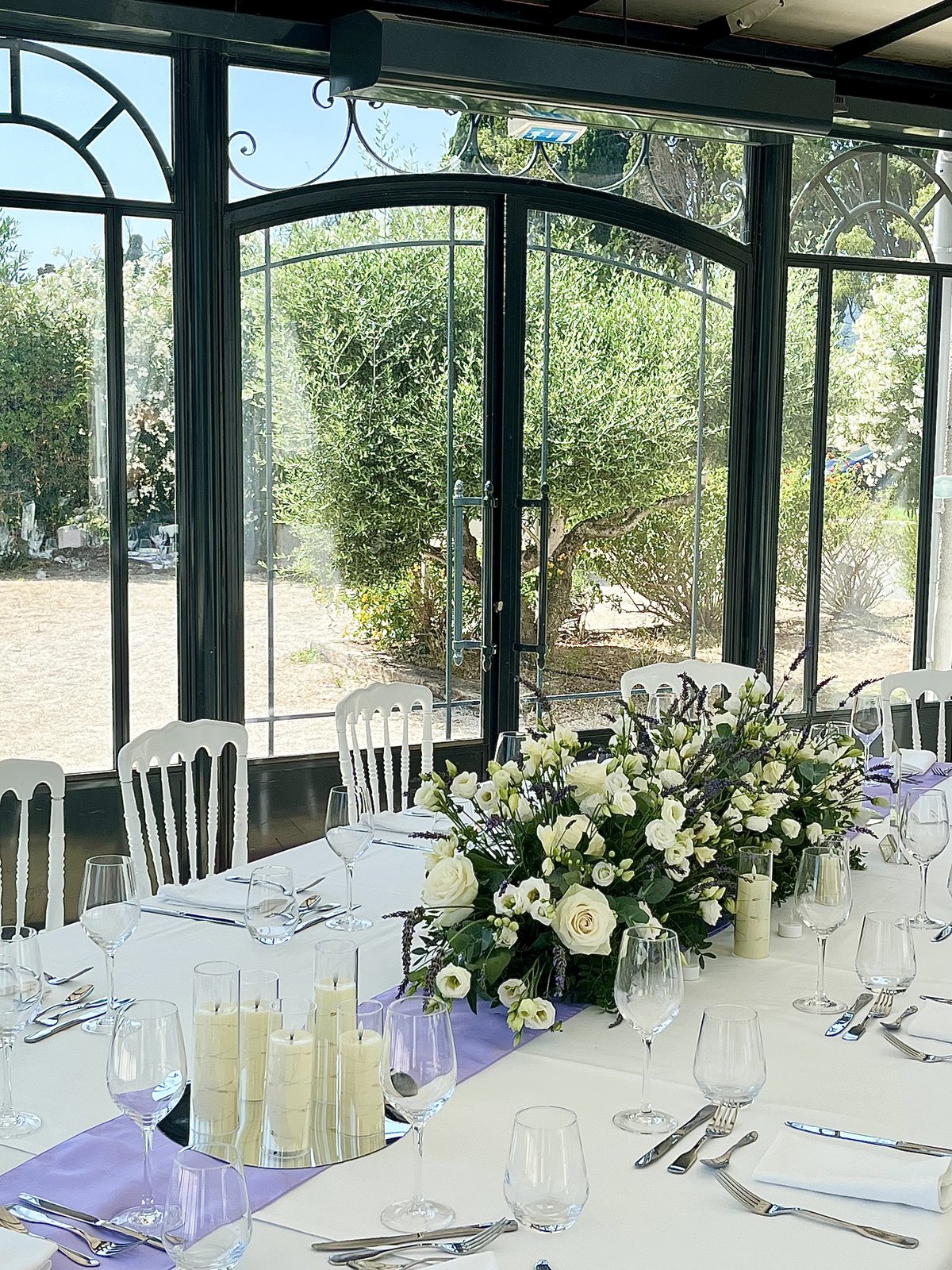 Centre de table blanc et lavande dans une véranda avec vue sur un olivier