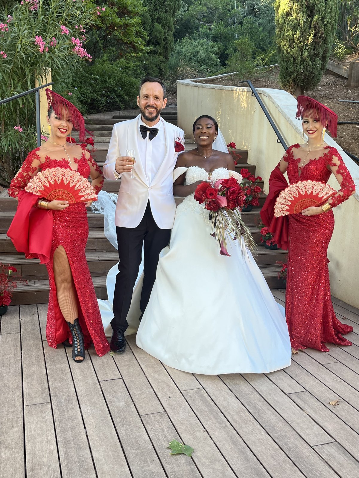 Mariés entourés de danseuses en robes rouges avec éventails, bouquet de roses rouges