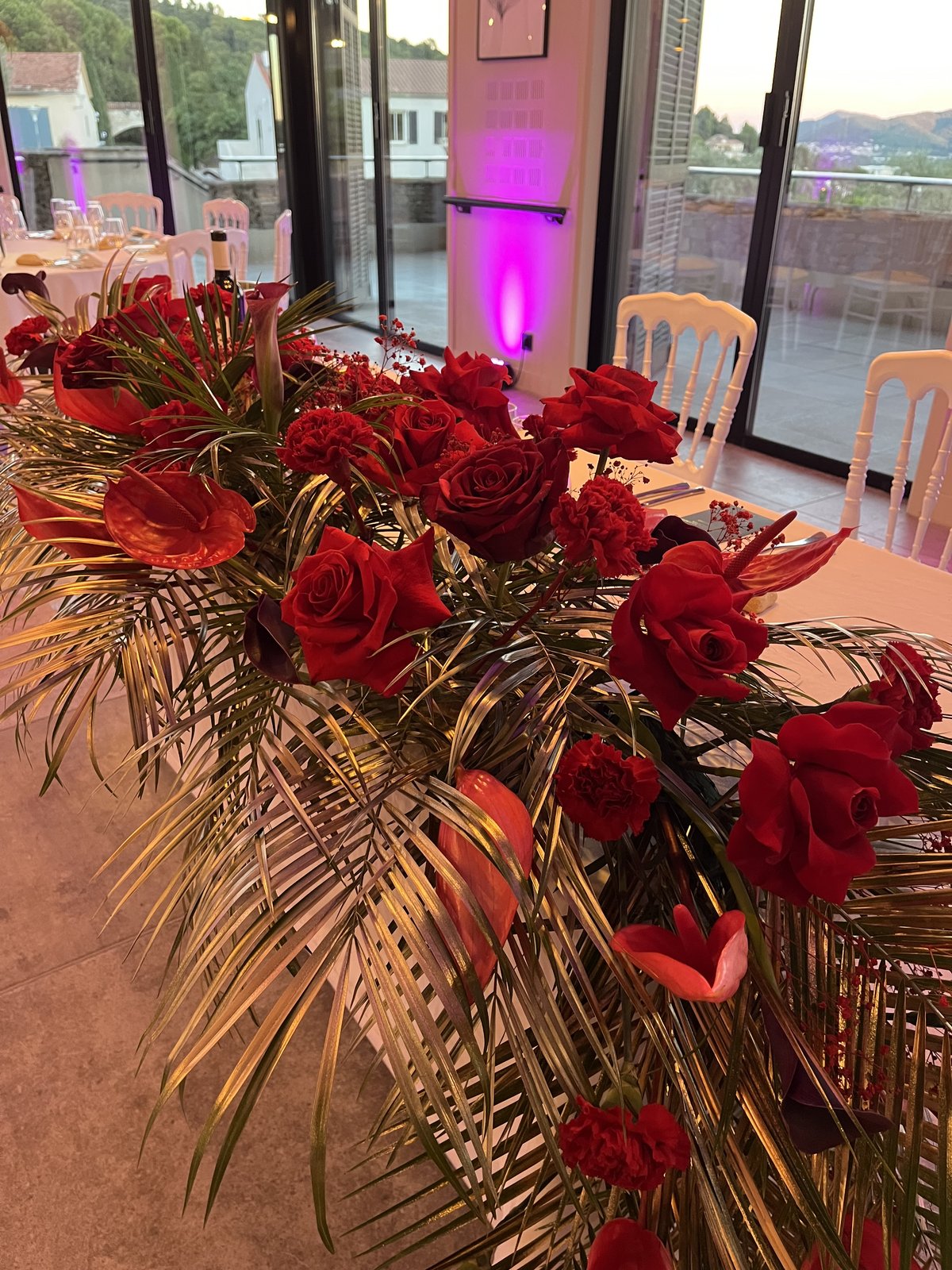 Détail d'une composition de roses rouges et feuillage doré sur une table de mariage