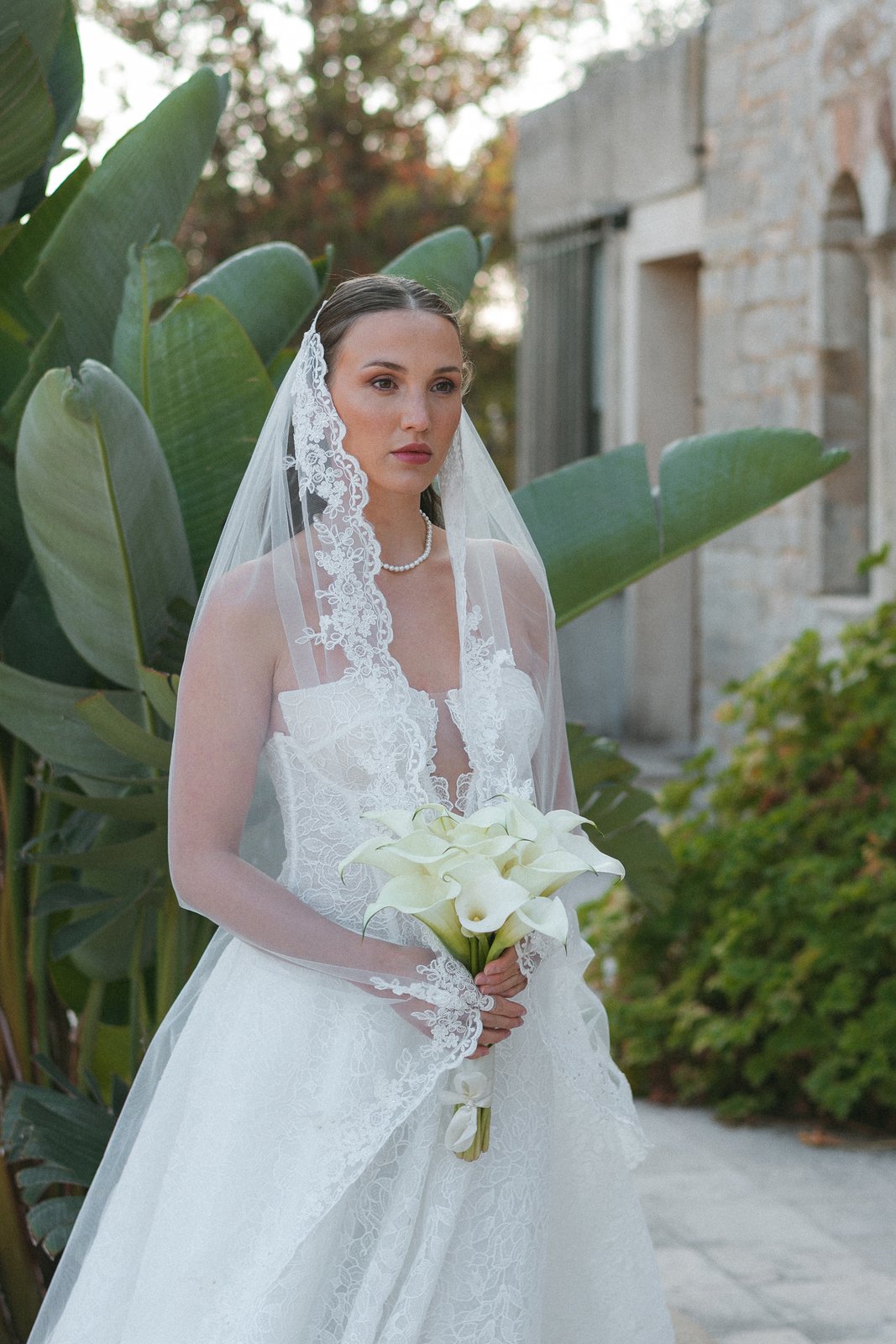 Mariée en voile tenant un bouquet de callas blancs devant un feuillage tropical